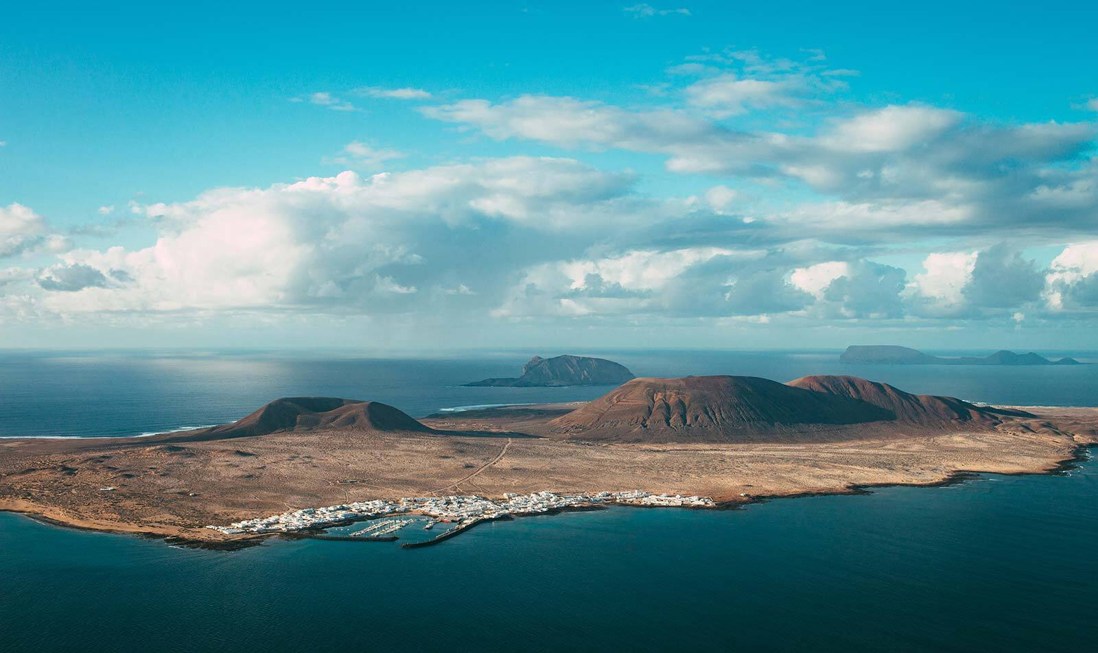 Widok z Lanzarote na wyspę La Graciosa, wulkaniczne wzgórza i nadmorską miejscowość otoczoną wodami Atlantyku.